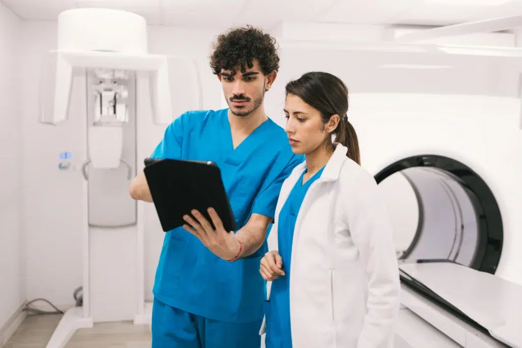 Two clinicians reviewing patient records near a radiation therapy machine, reflecting the documentation behind radiation oncology billing services