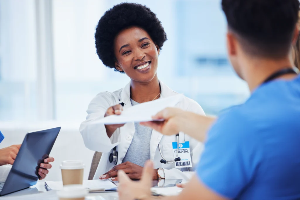 Healthcare colleagues passing a document across a table, representing the paperwork behind a single case agreement with a payer